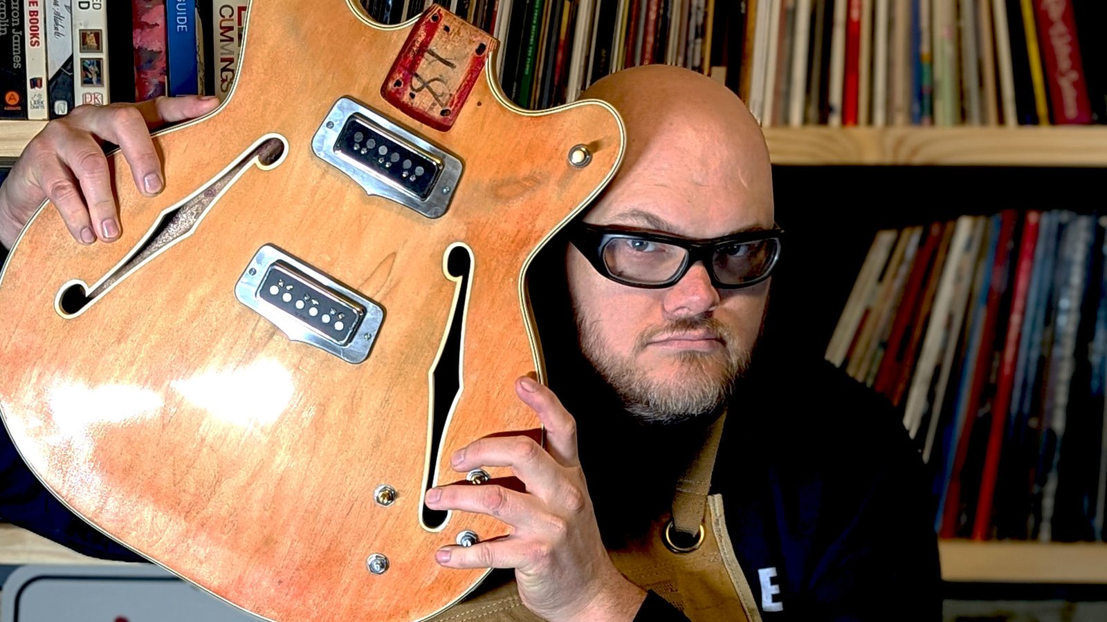 John peering out from behind the worn, stripped body of a vintage hollow-body guitar.